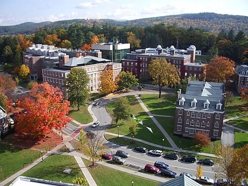 Aerial view of Dartmouth College’s campus green ringed by brick academic buildings and hills of autumn foliage.