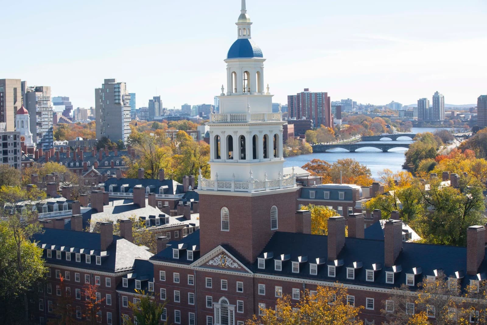 Aerial view of Harvard’s Lowell House bell tower with the Charles River, Boston skyline, and autumn foliage in the background.
